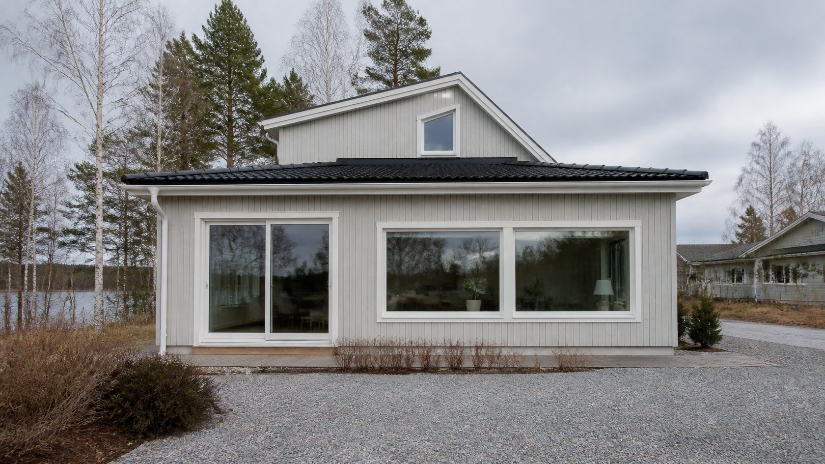 Nybyggd ljusgrå trätillbyggnad med stora fönster på ett svenskt villahus vid sjön – slutbesked