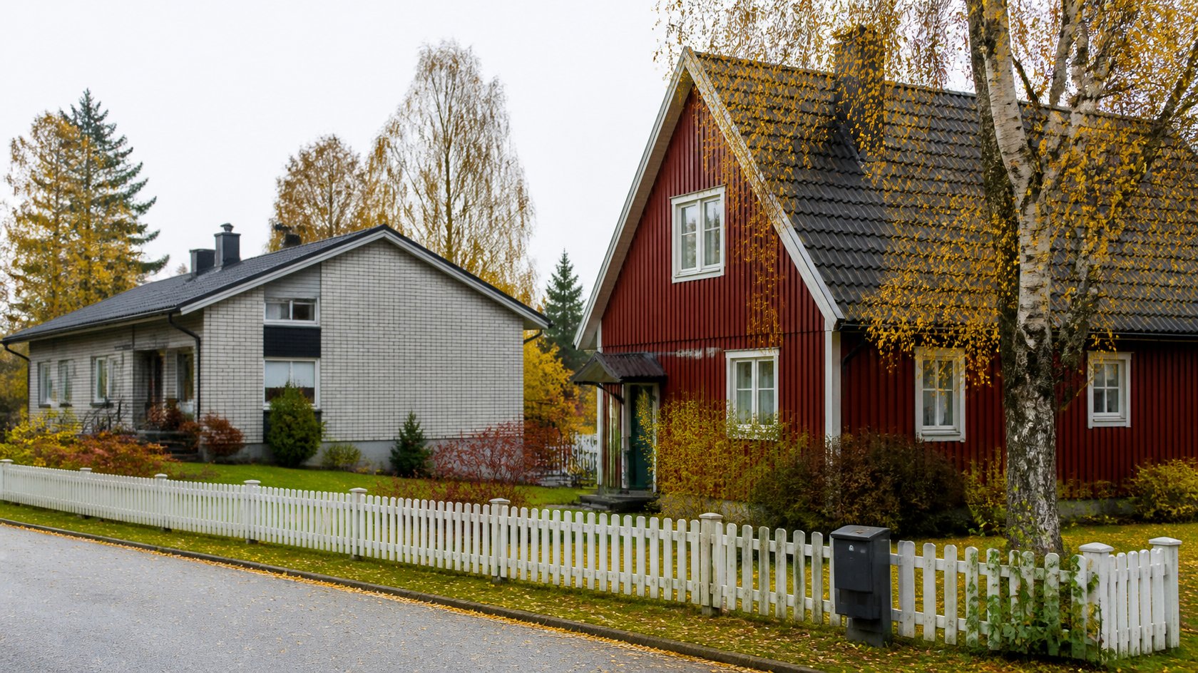 Röd trävilla och ljus tegelvilla med vitt staket i ett svenskt villaområde en höstdag